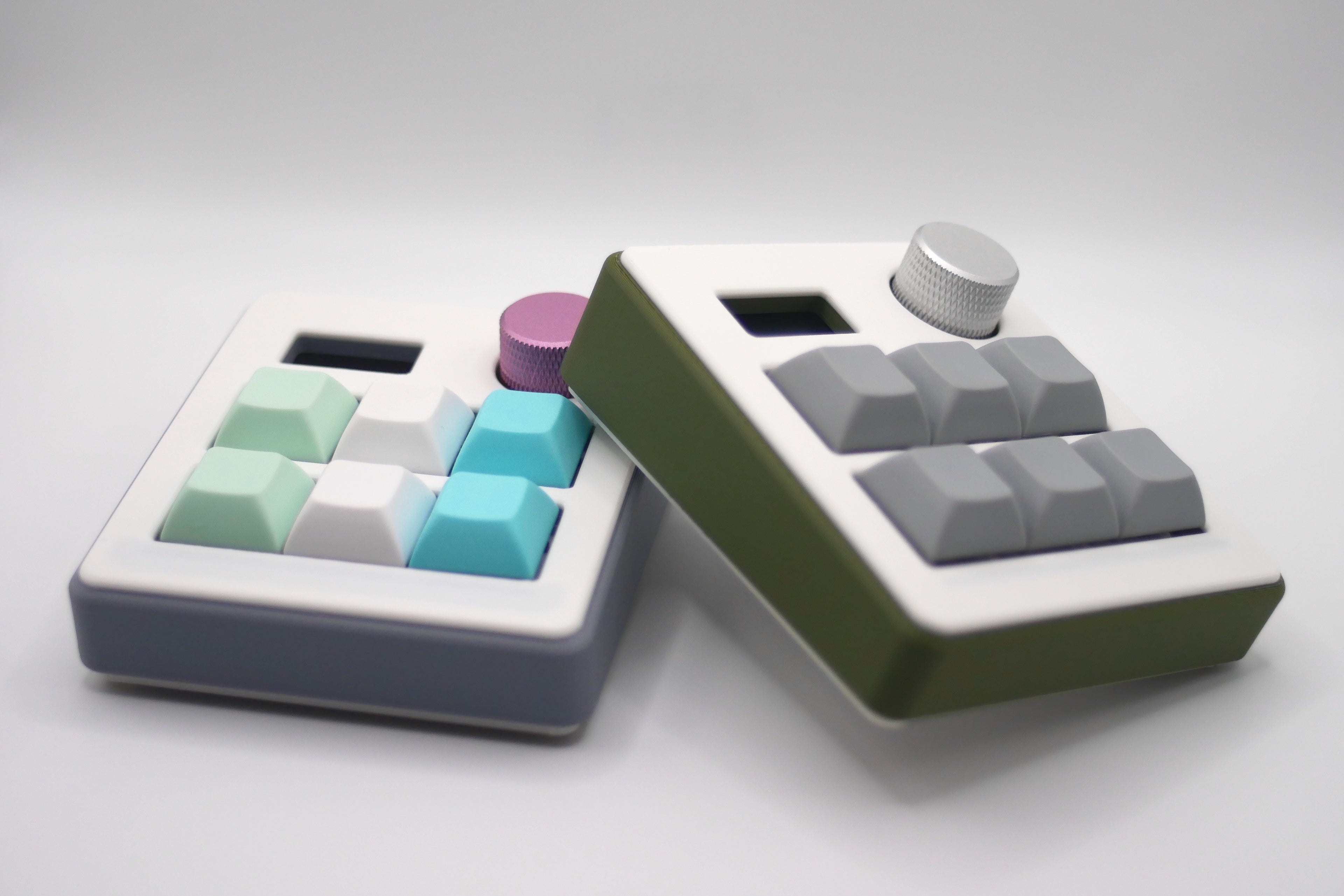 Two customizable 6-Key macropads with a volume knob and screen in green and gray with mint green, white, gray, and teal keycaps made by TogKey