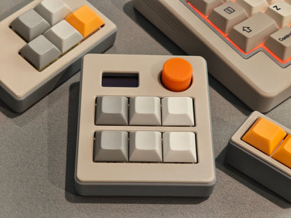 Close-up of a mechanical keyboard with beige and orange keycaps on a gray surface.
